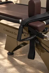 Close view of bronze frame, brown upholstery, handle, strap, and Carriage Co branding